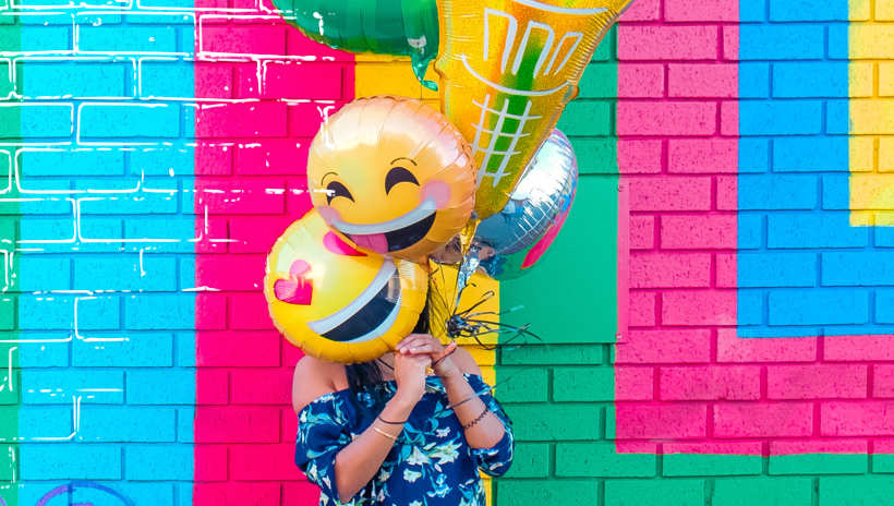 mujer aguantando globos de helio de emojis felizes
